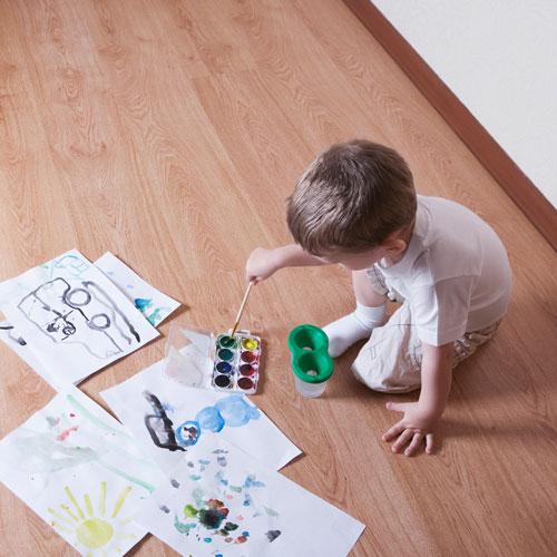 Boy with painting materials on laminate flooring